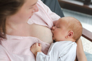 A white skinned, brown haired woman wearing a pink shirt breastfeeds her newborn baby