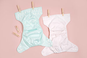 Two cloth nappies laid out flat on a pale pink background.