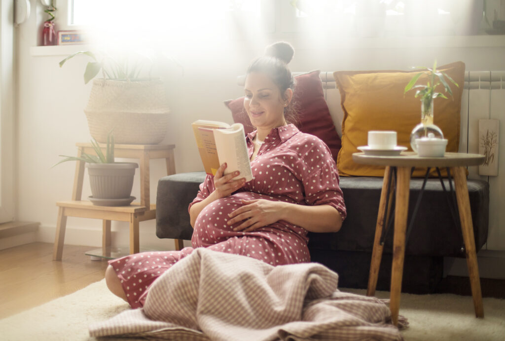 A pregnant woman is sitting on the floor reading and caressing her bump